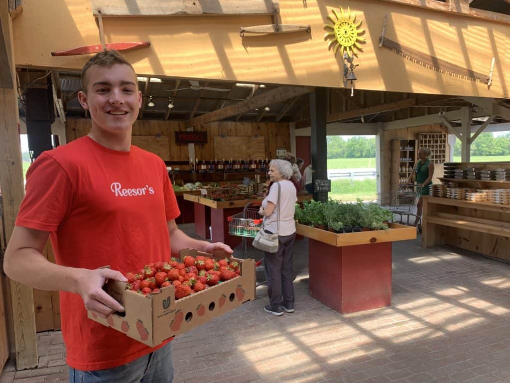 Fresh strawberries at a local farmer's market with wooden displays and bright natural lighting.