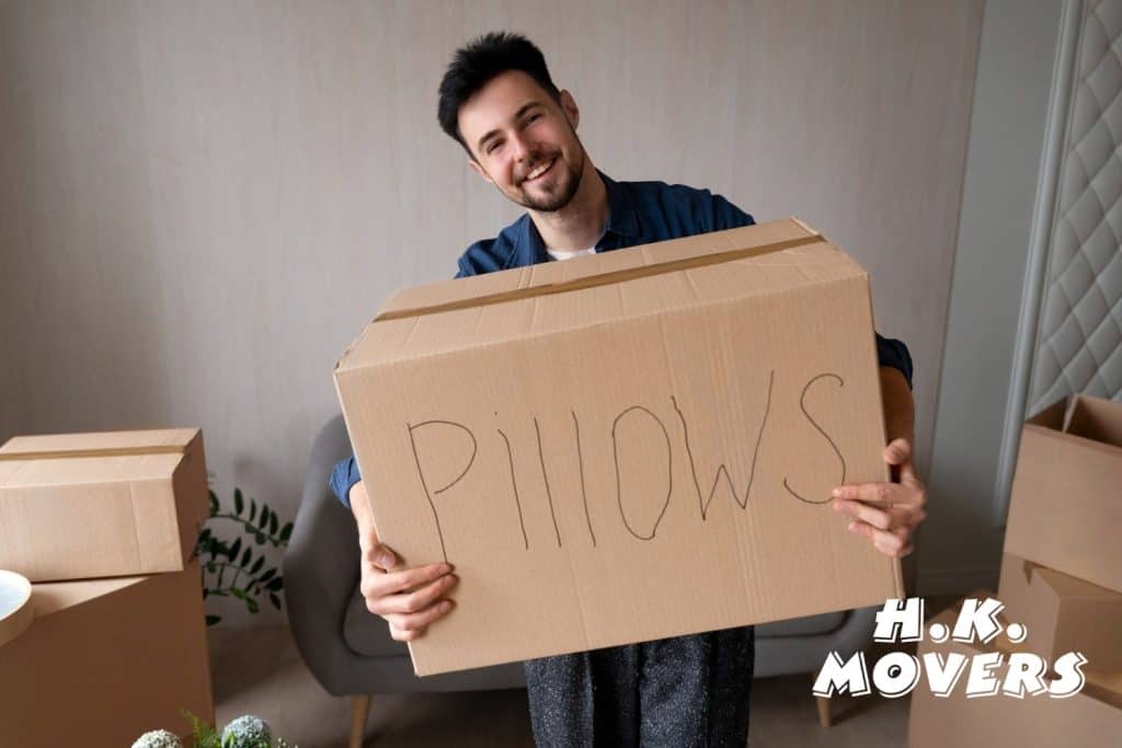 Professional moving company staff holding a cardboard box labeled "PILLOWS" during a residential move, showcasing reliable and efficient local and long-distance moving services.