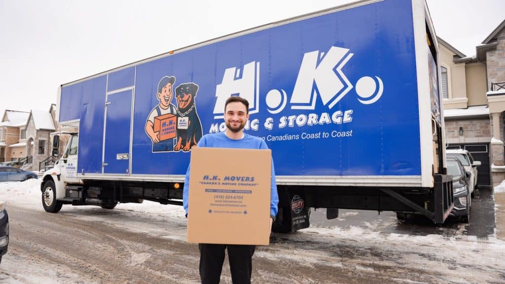 Mover holding box near moving truck in winter