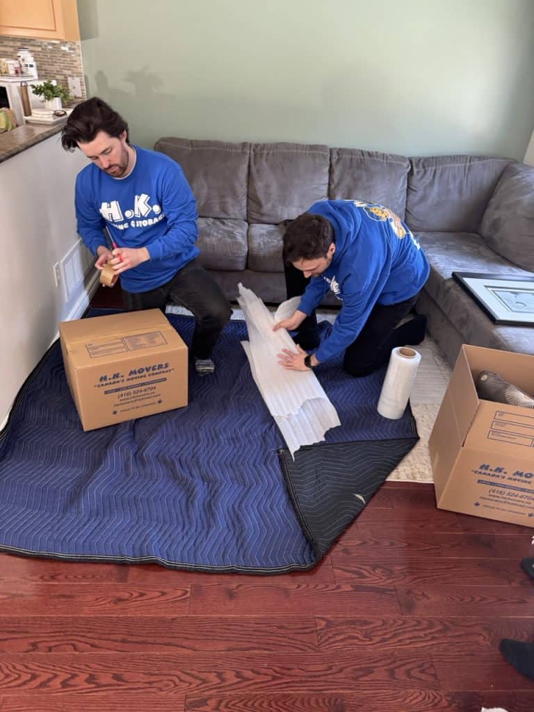 Professional movers from HK Movers organizing packing supplies on a living room floor.